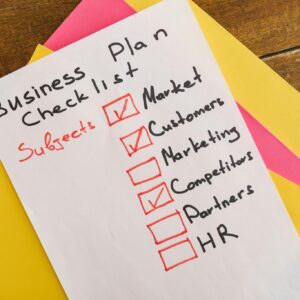A handwritten business plan checklist on a table with colorful papers indicating important topics for startups.