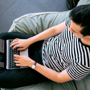 A man in a striped shirt using a laptop on a bean bag, embodying relaxed productivity.