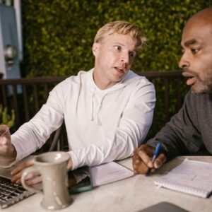 Two men collaborating on a project with a laptop outdoors, discussing ideas.